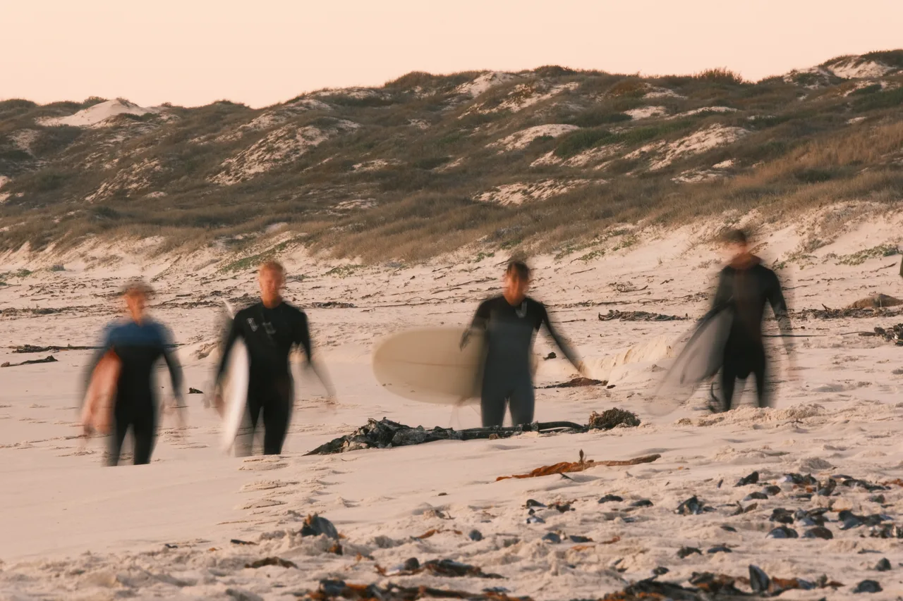 Four surfers blurred in motion as they walk along a beach.