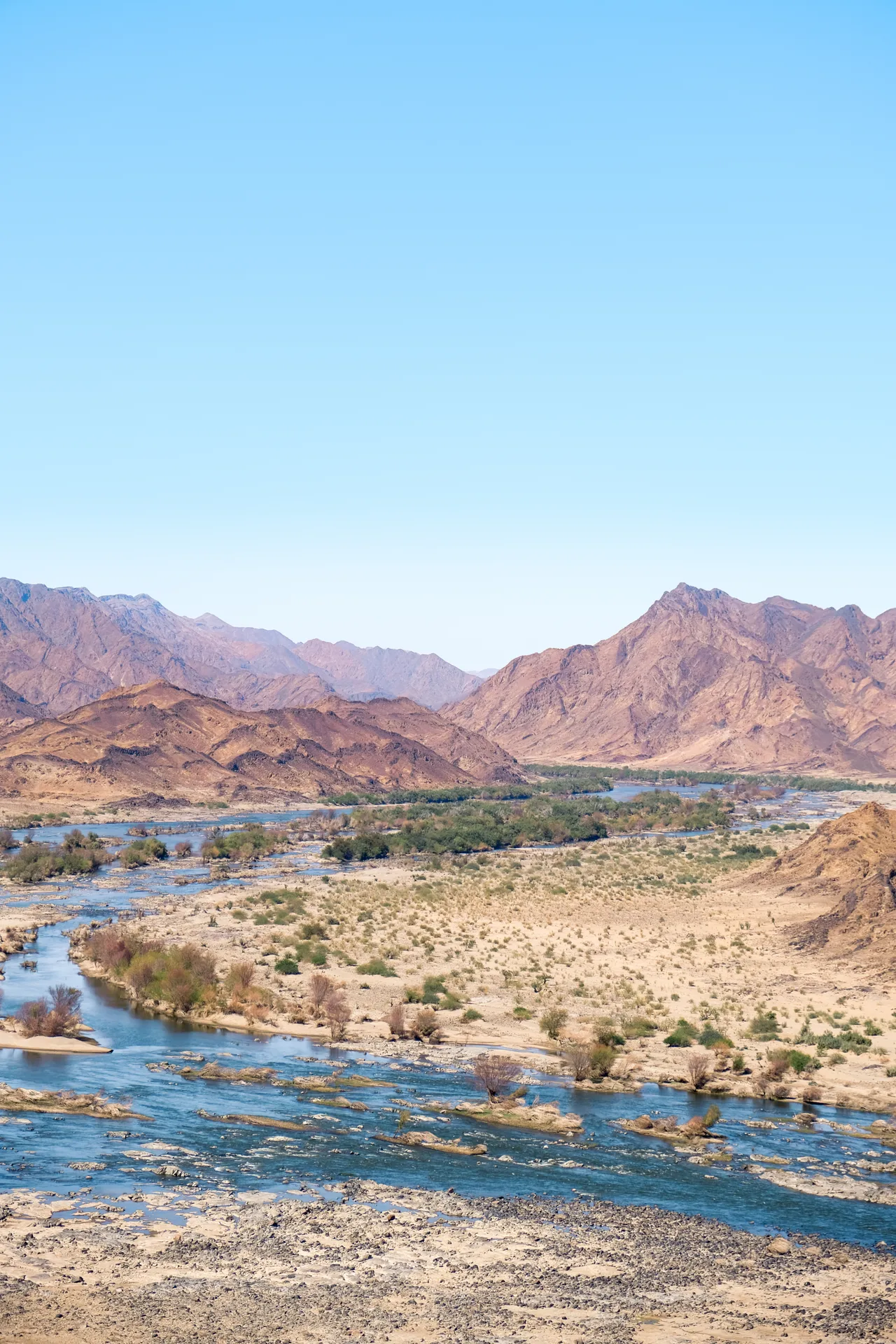 A river winding through a rocky mountain valley under a clear sky.
